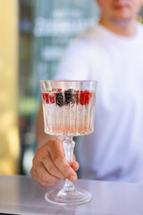 Bartender serving cocktail with fresh berries and ice, Close-up of bartender presenting a chilled cocktail in an elegant glass with ice cubes, raspberries, and blackberries, highlighting mixology and 