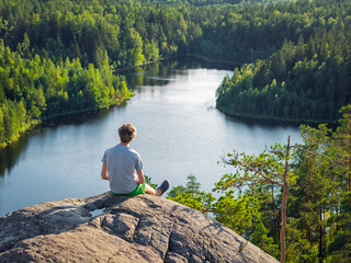 A man sits on a rock and contemplates a forest lake