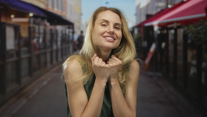 Woman smiling on city street making come gesture in bright daylight, embodying youthful energy and...