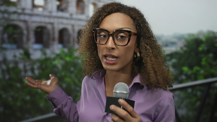 Transgender woman holding microphone with finger pointing to microphone at outdoor roman building;...