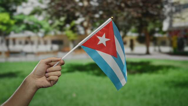 Caucasian man holding a cuban flag in a park setting, showcasing national pride and identity amidst a vibrant outdoor environment.