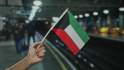 Man holding kuwaiti flag at indoor train station, capturing diverse commuter environment with...