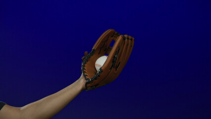 Man catching baseball with glove in front of a vibrant blue background, emphasizing the sport...