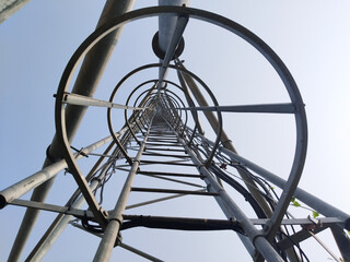 Upward view of steel tower with circular safety rings and climbing ladder, industrial iron...