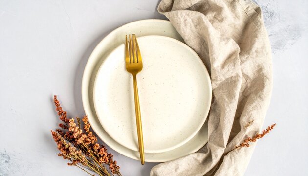 Elegant table setting with an empty speckled white plate, a gold fork, and a beige linen napkin, decorated with dried flowers in a flatlay style