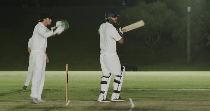 Bowler delivering Diverse team missing shot catching appealing wicket on pitch at night, copy space