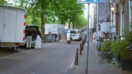 Blurred city street scene with people near a vehicle, bicycles, and trees, in a european urban area...