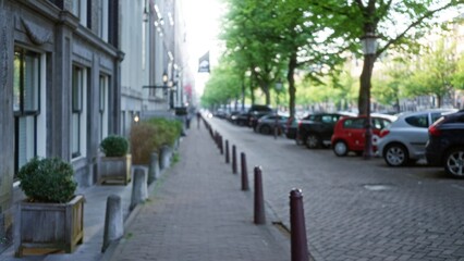 Defocused view of a european city street with parked cars, lined with trees and historic buildings,...