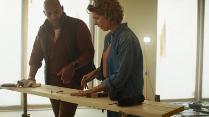 A man and woman discuss home renovation plans, measuring wood and pointing towards areas of interest in a landscape, medium shot.