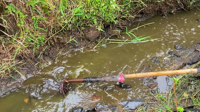 Close-up of a volunteer cleaning a muddy gutter with a hooked tool, promoting flood prevention and environmental awareness through community action.