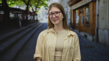 Young blonde woman wearing glasses smiling and looking up on a bustling city street; optimism...