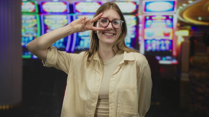 Woman confidently flashes peace sign with hand over eye at brightly lit slot machine in casino...