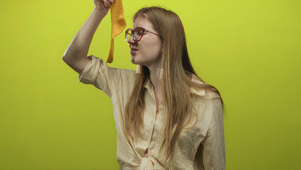 Woman holding yellow sock inspects it while lifting her hand in lime green studio with glasses on;...