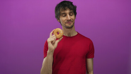 Man wearing red tshirt holding glazed donut with one hand and making ok sign with other in purple...