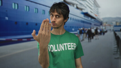 Young volunteer man finger pointing directly at camera at port terminal; community service drive...