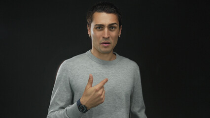 Young man with hand on chest wearing a watch, expressing emotion against an isolated black...