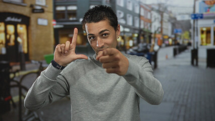 Young hispanic man making loser gesture with hand and pointing at camera in busy urban street;...