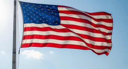 Obraz premium Waving Flag with Stars and Stripes on Metal Pole Against Bright Blue Sky