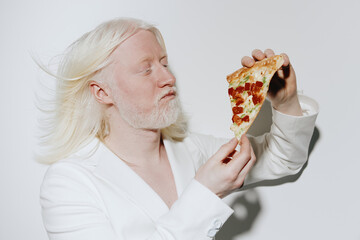 Person enjoying pizza with a focused expression, wearing a white suit against a minimalist white...