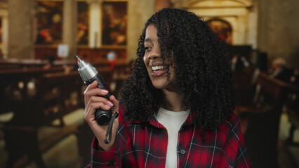 African american woman holding drill with right hand and smiling in church interior; confidence...