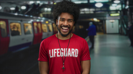 Lifeguard man in a red shirt smiling at a busy indoor train station with blurred commuters and a...
