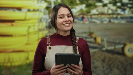Young woman in apron holds a tablet by the beach, showcasing a casual seaside atmosphere with...
