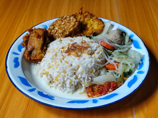 A portion of typical Indonesian mixed rice is served on a classic enamel plate with a blue and...