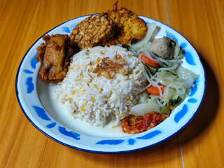 A portion of typical Indonesian mixed rice is served on a classic enamel plate with a blue and...
