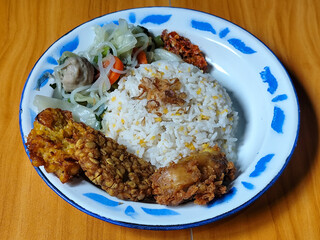 A portion of typical Indonesian mixed rice is served on a classic enamel plate with a blue and...