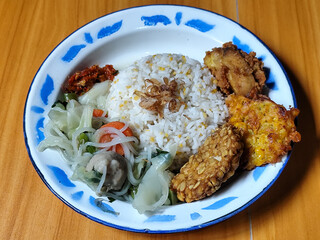 A portion of typical Indonesian mixed rice is served on a classic enamel plate with a blue and...