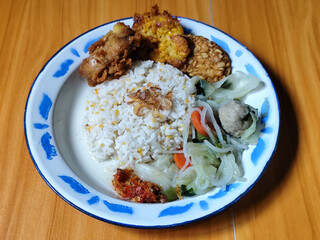 A portion of typical Indonesian mixed rice is served on a classic enamel plate with a blue and...