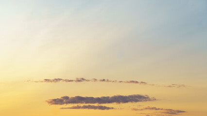 Thin clouds stretch across a golden-yellow sky at dusk, with soft gradients fading into pale blue...