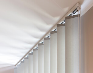 The top section of beige vertical blinds is shown in detail, highlighting the rail and control...