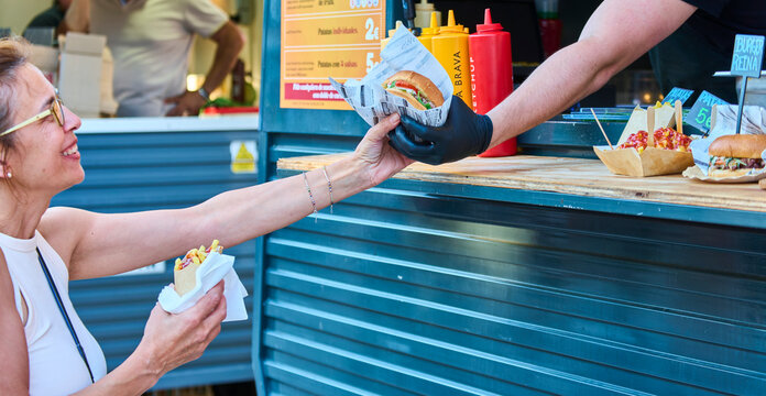 Close-up of happy woman grabbing a hamburger during a hamburger food truck festival. - Powered by Adobe