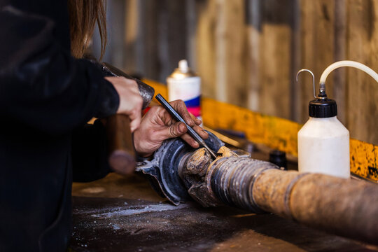 Female mechanic hand striking the chisel with a hammer over the vehicle drive shaft