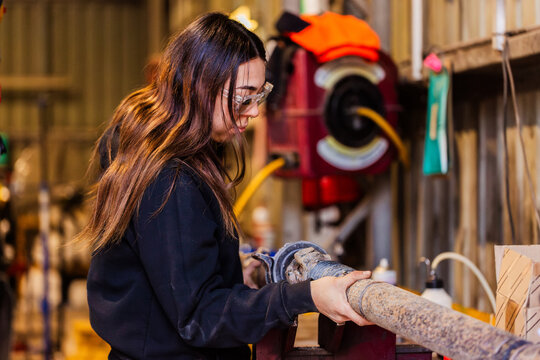 Female mechanic checking and repairing vehicle drive shaft in industrial workshop
