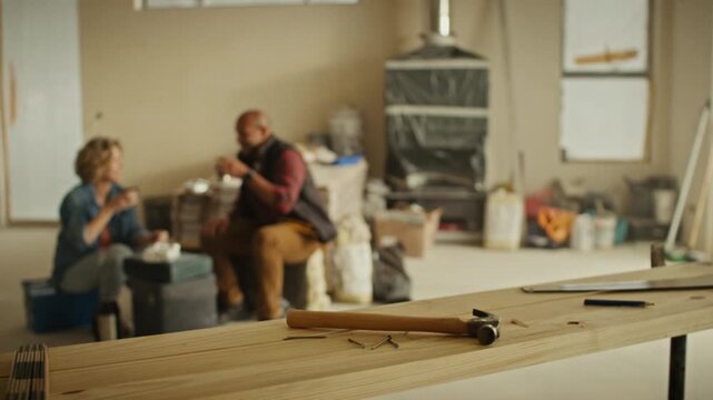A middle-aged man and woman sit and discuss their home renovation project, taking a break, with tools in the foreground.