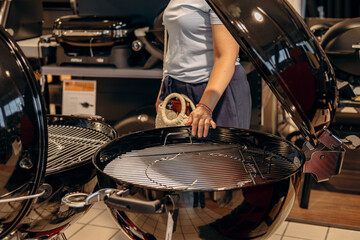 Obraz premium Woman inspecting modern charcoal grill in a retail store, showcasing sleek design and functionality for outdoor cooking enthusiasts