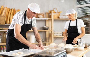 Two bakers place pieces of dough on a baking tray to make croissants