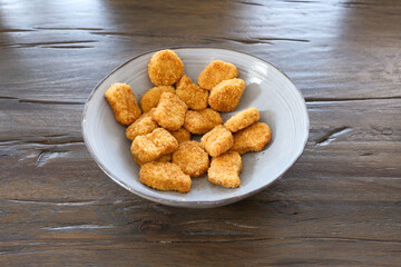 A bowl of chicken nuggets sits on a wooden table