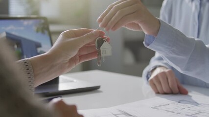Hands of female real estate agent giving keys to client over office desk with architectural plans and laptop during property ownership transfer. Close-up view - Powered by Adobe