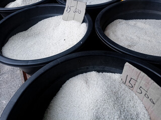 Raw white rice sold in bulk at a local market, stored in round black tubs