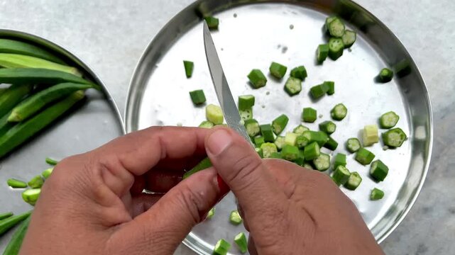 Close-up video of an Indian woman cutting fresh green okra (ladyfinger) with a knife, ideal for cooking, kitchen preparation, and traditional Indian cuisine concepts.