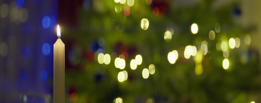 A wax candle is burning on the background of a Christmas tree with a garland