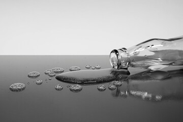 A black and white image of a spilled bottle and a puddle on a reflective surface