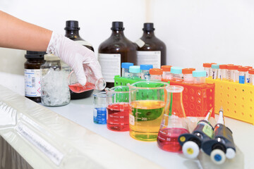 Scientist pouring the red solution in the flask into the blue solution in the beaker at the chemical laboratory.