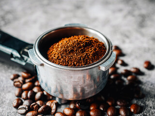 Close-up ground coffee in portafilter and roasted coffee beans or filter coffee handle on gray background