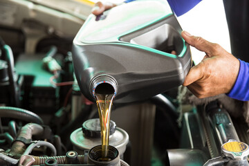Car mechanic replacing and pouring fresh oil into engine at maintenance repair service station