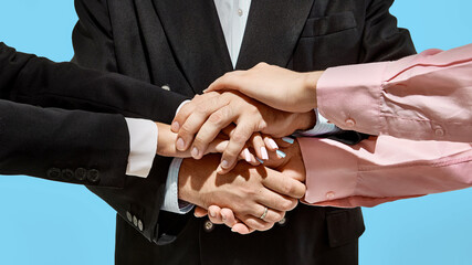 Close-up of diverse business team showing unity with hands stacked together on vibrant blue...
