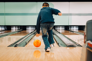 Teenage boy mid-roll while ten pin bowling in brightly lit bowling alley
